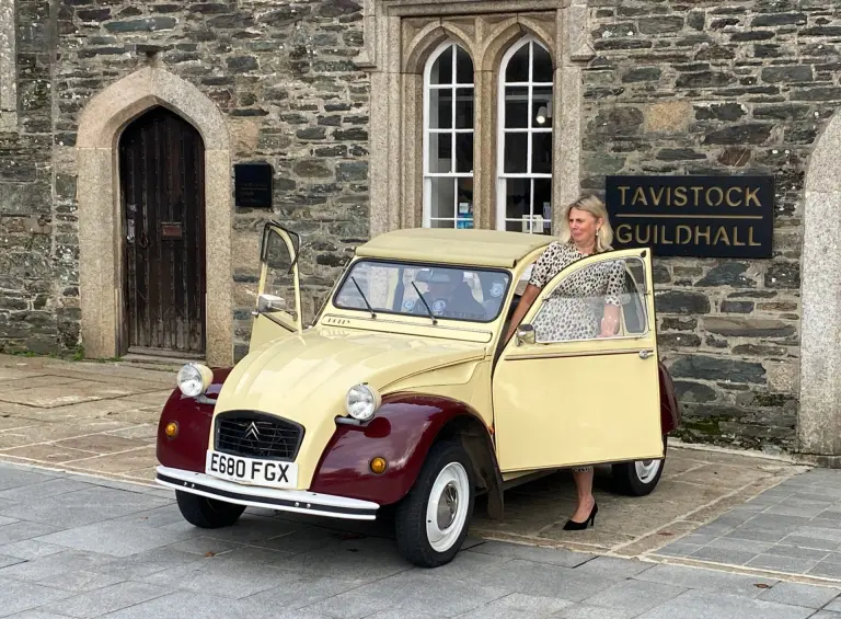 Cream and maroon Citroën 2CV E680 FGX at Tavistock Guildhall for the Antiques Roadshow, a woman beside its open door